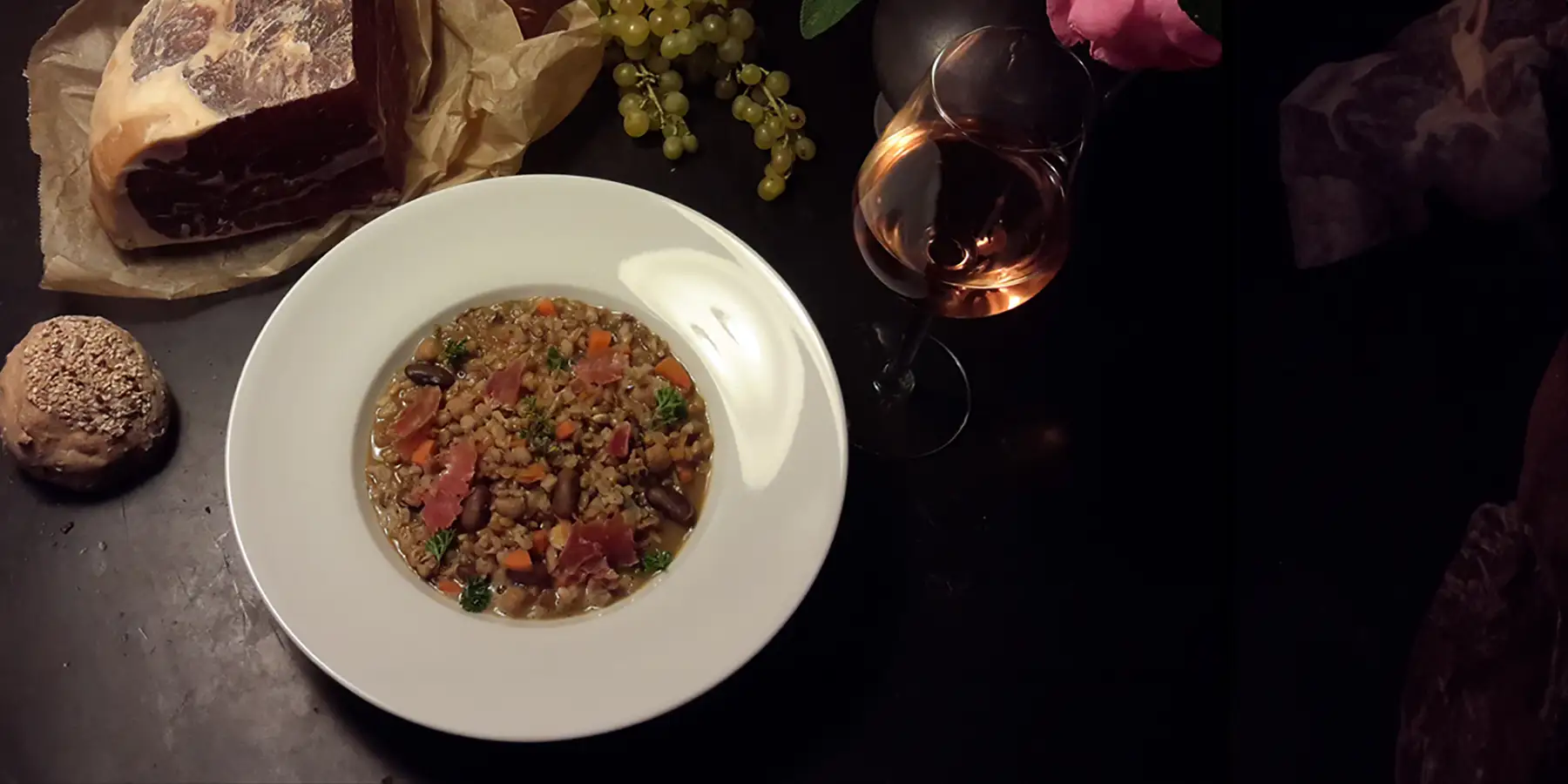 Teller mit einer italienischen Dinkelsuppe, auch bekannt als Minestra di Farro, auf einem Tisch mit Brot, Weintrauben und Wein.